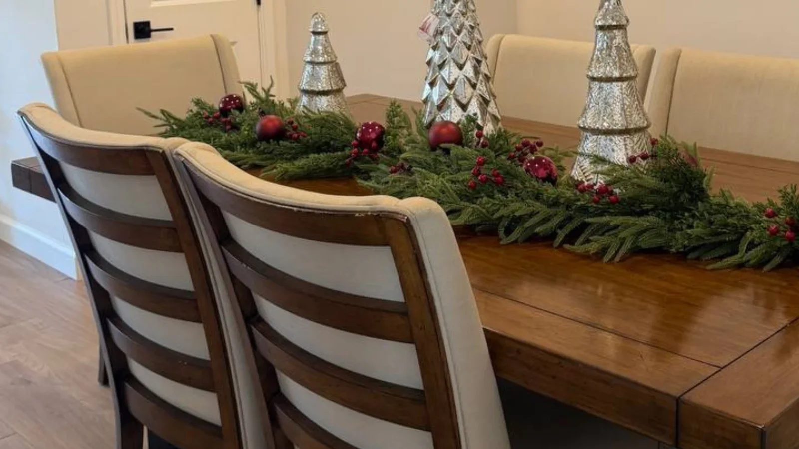 Mesa de comedor de madera decorada para Navidad con camino de ramas verdes, esferas rojas y árboles plateados
