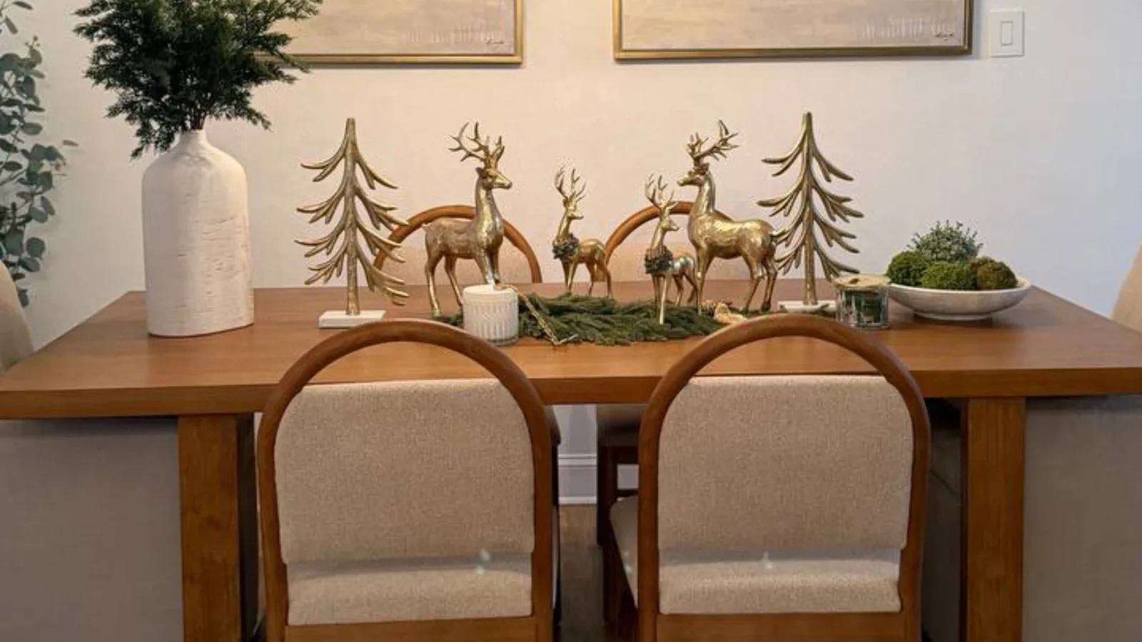 Mesa de comedor con centro navideño de renos y árboles dorados sobre un camino de ramas verdes